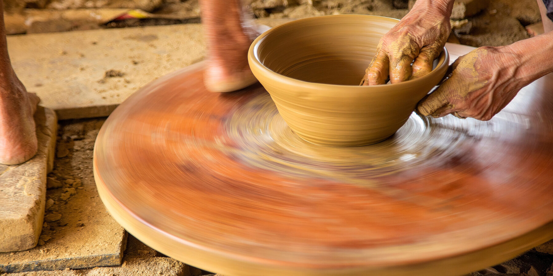 Two,Women,Work,On,A,Pottery,Wheel,,One,Pedaling,The